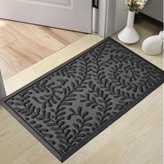 a door mat that is on the floor next to a vase with flowers in it