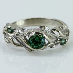 a close up of a ring with a green stone in the center and leaves around it