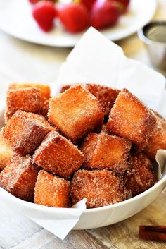 a bowl filled with sugared croutons on top of a table next to strawberries