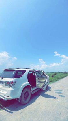 a white car with its door open sitting on the side of a road next to grass