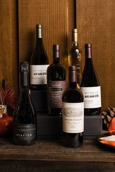 several bottles of wine sitting on top of a wooden table next to an apple and pine cone