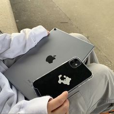 a person holding an apple laptop computer in their lap and sitting on the ground with it's lid open