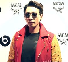 a young man wearing sunglasses and a red jacket standing in front of a microphone with his hand on his hip