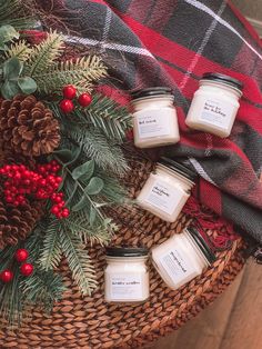 four candles sitting on top of a basket next to pine cones and evergreen branches with red berries