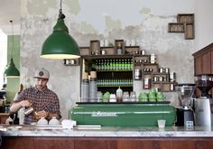 a man sitting at a counter in front of a green coffee maker and some cups