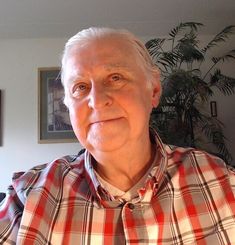 an older man with white hair wearing a red and white plaid shirt looking at the camera