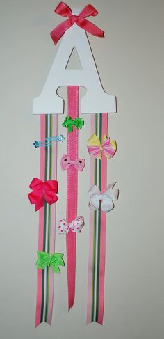 a pink and green striped wall hanging with bows on it's sides, featuring the letter a