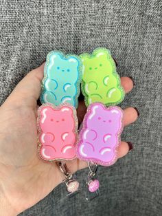 someone is holding three small bear shaped keychains in their left hand and the other one has a pink, green, blue, and yellow teddy bear on it