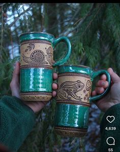 two hands holding green and gold mugs in front of pine tree with snow on ground