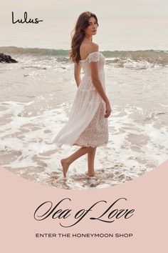 a woman in a white dress walking on the beach with her feet in the water