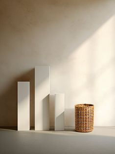 a basket sitting next to three tall white boxes on the floor in front of a wall