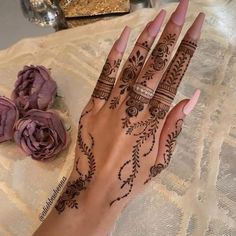 a woman's hand with henna tattoos on it and flowers in the background