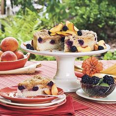 there is a cake on the table with berries and peaches around it, along with other desserts