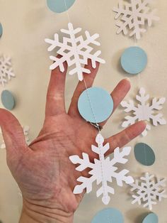 a hand is holding some paper snowflakes in front of blue and white confetti