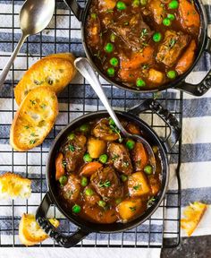 two pans filled with stew on top of a table next to slices of bread