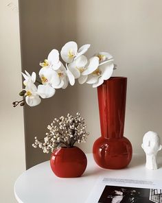 two red vases with white flowers in them on a table next to a magazine