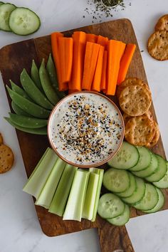 carrots, celery and crackers are arranged on a cutting board with dip