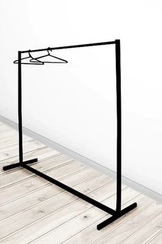 a black metal frame with clothes hanging on it's sides in front of a white wall