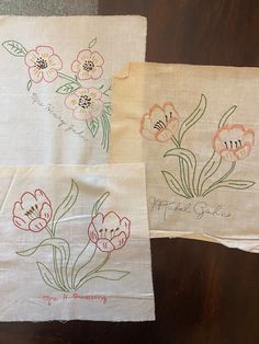 three embroidered napkins with flowers on them sitting on a wooden table next to each other