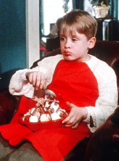 a young boy sitting in a chair holding a plate of food with marshmallows on it