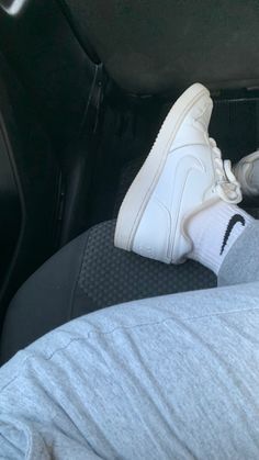 a person's feet wearing white sneakers in the back seat of a car