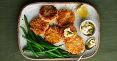 a white plate topped with green beans and fried meat next to dipping sauces on top of it