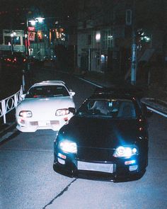 two cars are parked on the side of the road at night, one is white and the other is black