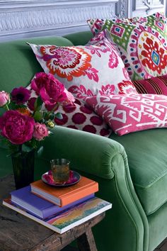 a green couch with colorful pillows on top of it next to a coffee table and vase