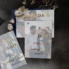 two save the dates cards with gold foil on them next to an envelope and tie