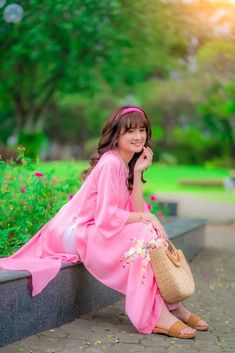 a woman in a pink dress is sitting on a bench and talking on her cell phone