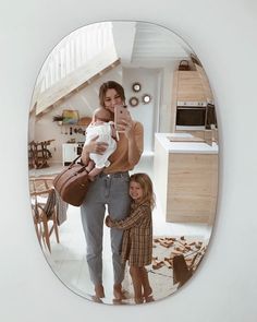 a woman holding a baby and taking a selfie with her cell phone in the mirror