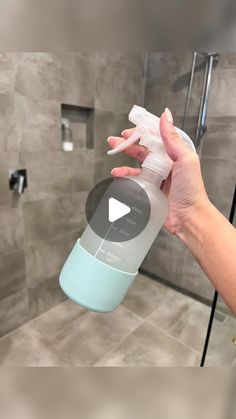 a hand holding a spray bottle in front of a tiled shower area with gray tiles