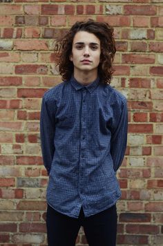 a man standing in front of a brick wall wearing a blue shirt and black pants