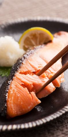 salmon with chopsticks on a black plate next to rice and lemon wedges