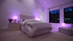 a large white bed sitting in a bedroom next to two night stands with purple lights on them