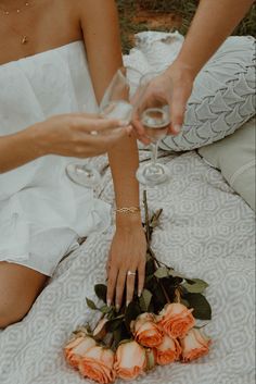 two women sitting on the ground holding wine glasses and flowers in front of each other