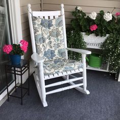 a white rocking chair sitting on top of a blue carpeted porch next to potted plants