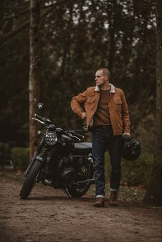 a man standing next to his motorcycle in the woods