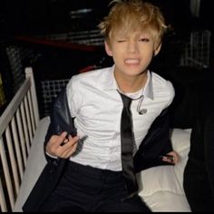 a young man wearing a white shirt and black tie sitting on a bench with his eyes closed