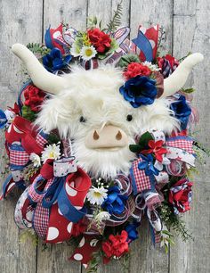 a stuffed cow with red, white and blue flowers on it's head sits in the middle of a wreath