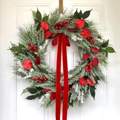 a wreath with red flowers and greenery hanging on a white front door decorated for christmas