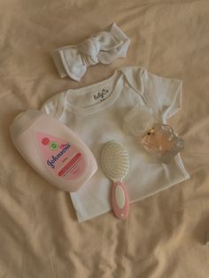 baby items laid out on a bed with a white shirt and pink hairbrush next to it