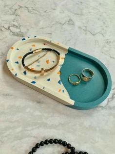 two rings and bracelets in a tray on a marble counter top next to a beaded bracelet