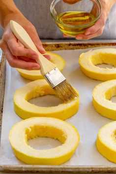 someone using a brush to paint the inside of squash rings on a baking sheet with oil