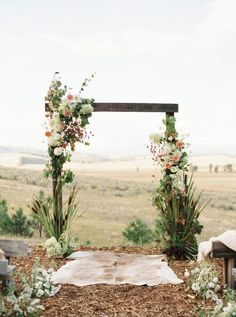 an outdoor ceremony setup with flowers and greenery on the ground in front of a field