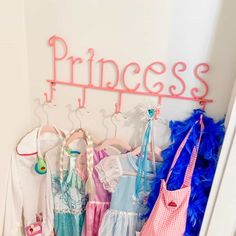 there is a pink princess sign on the wall next to many other dresses and purses