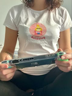 a woman sitting on the floor holding a nintendo wii game controller in one hand and a cell phone in the other