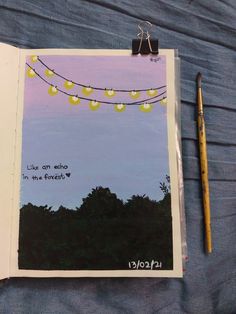 an open notebook with a string of lights hanging from it's side next to a pencil