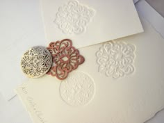 two white envelopes with intricate designs on them, one is open and the other has a button