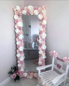 a white rocking chair sitting in front of a mirror with flowers on the wall above it